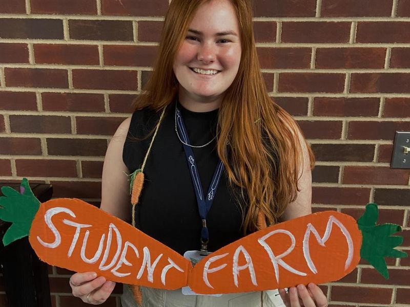 A person holds a sign that says Student Farm in front of a brick wall